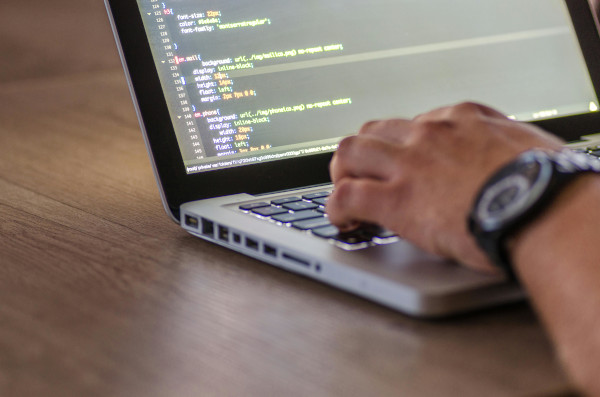 An image of a person's wrist in front of a monitor showing code.